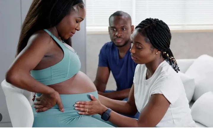 Pregnant woman receiving antenatal care from a healthcare worker with a partner nearby in a clinical setting.