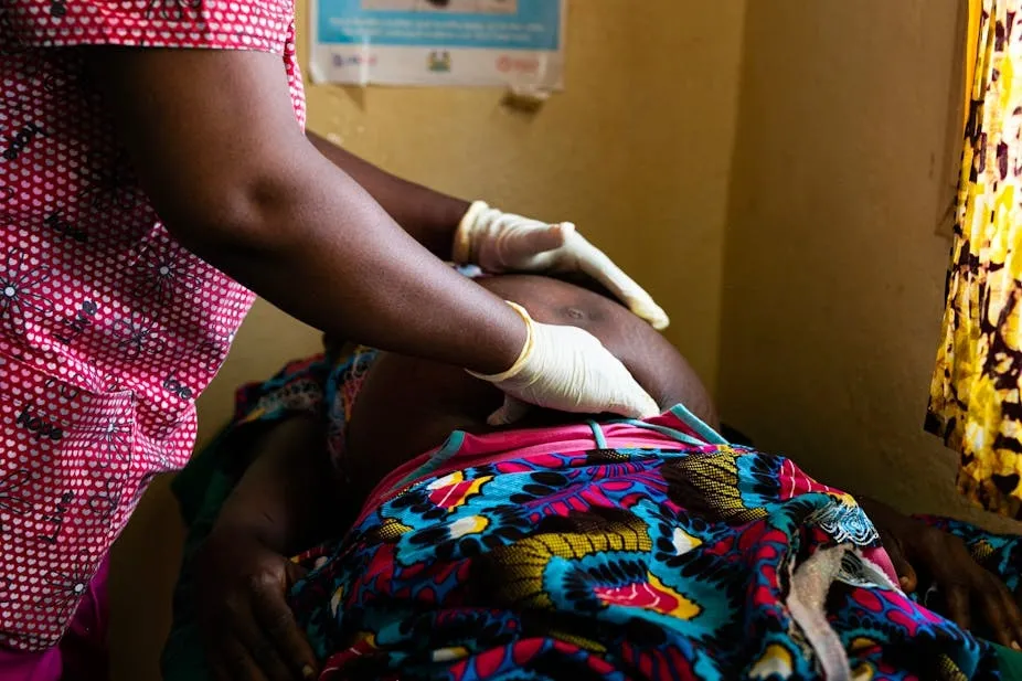 Healthcare worker in gloves examines a pregnant woman's belly during a maternal health checkup in Ghana.